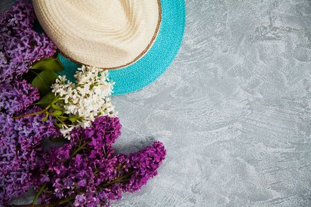Summer hat and lilac blooming branches on grey background. Copy space for text, spring concept.の写真素材