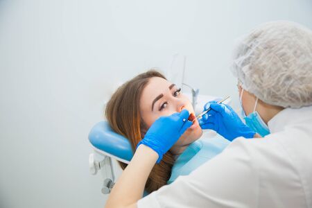 Female dentist curing teeth cavity in blue gloves and protective mask. Dentist caries treatment at dental clinic office. People, medicine, stomatology and health care conceptの写真素材