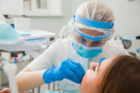 Female dentist curing teeth cavity in blue gloves and protective mask. Dentist caries treatment at dental clinic office. People, medicine, stomatology and health care conceptの写真素材