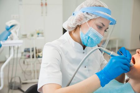 Female dentist curing teeth cavity in blue gloves and protective mask. Dentist caries treatment at dental clinic office. People, medicine, stomatology and health care conceptの写真素材