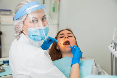 Female dentist curing teeth cavity in blue gloves and protective mask. Dentist caries treatment at dental clinic office. People, medicine, stomatology and health care conceptの写真素材
