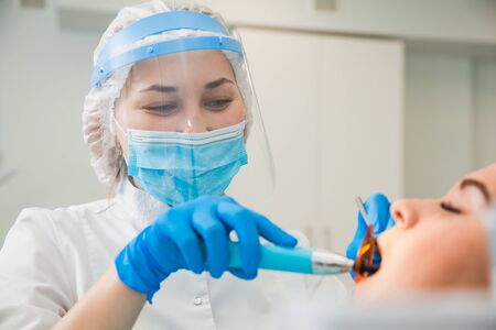 Female dentist work with light-curing seal, patient with caries on chair. Stomatologist and patient at clinical office. Toothcare conceptの写真素材