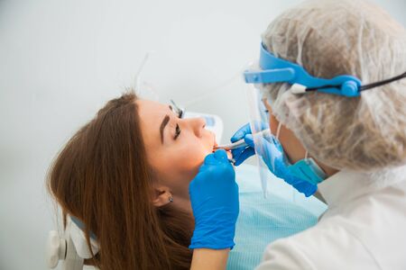 Female dentist work with light-curing seal, patient with caries on chair. Stomatologist and patient at clinical office. Toothcare conceptの写真素材