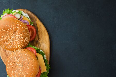 Tasty sesame buns with grilled beef burger, served with tomato, cheese and onions. Fast unhealthy food concept.の写真素材
