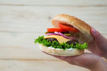 Hands holding homemade beef burger on wooden table. Ready to eat tasty fast food hamberger. Unhealthy food concept.の写真素材