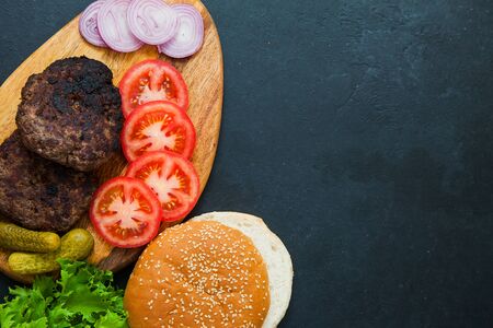 Set of beef burger ingredients on dark table. two cutlets, tomatoes, onions, salad and fresh sesame buns. Delicious homemade dish.の写真素材