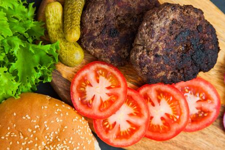 Set of beef burger ingredients on dark table. two cutlets, tomatoes, onions, salad and fresh sesame buns. Delicious homemade dish.の写真素材