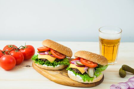 Two delicious burgers with beer and tomato branch on white wooden table. Fast food, junk eating concept.の写真素材