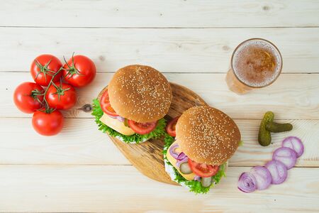 Two delicious burgers with beer and tomato branch on white wooden table. Fast food, junk eating concept.の写真素材
