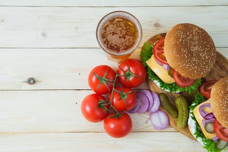 Two delicious burgers with beer and tomato branch on white wooden table. Fast food, junk eating concept.の写真素材