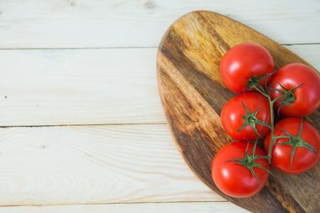 Fresh juicy tomato branch on wooden plate. Red vegetable on table. Vegetarian food, tasty product concept.の写真素材