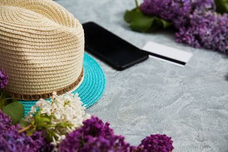Summer hat, smartphone, credit card and lilac blossom on grey background. Spring shopping concept, copy space for text.の写真素材