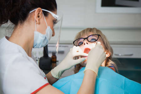 Closeup shot of dentist in protection mask working with tooth cavity and plague. Patient on stomatology chair repair aching teeth. Stomatologist and patient at clinic office. Toothcare conceptの写真素材