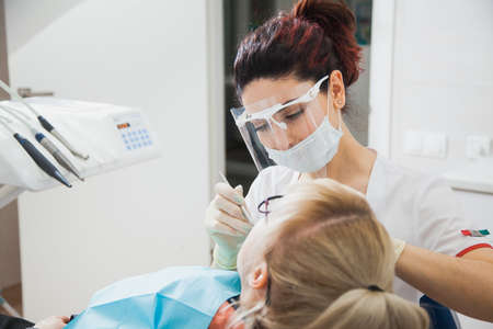 Closeup shot of dentist in protection mask working with tooth cavity and plague. Patient on stomatology chair repair aching teeth. Stomatologist and patient at clinic office. Toothcare conceptの写真素材