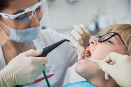 Dentist in protection mask washing mouth from tooth dust and blood. Patient on stomatology chair repair aching teeth. Stomatologist and patient at clinic office. Toothcare conceptの写真素材