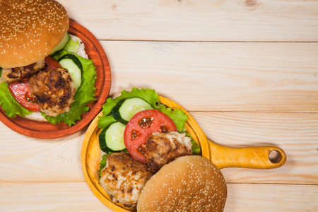 Two homemade hamburgers with fresh vegetables and chicken cutlets. Pair of burgers on handmade wooden serving pans. Delicious food on wooden table.の写真素材