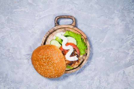 Craft homemade hamburger with fresh vegetables and chicken cutlet. Tasty burger on wooden hand carved serving wooden plate.の写真素材