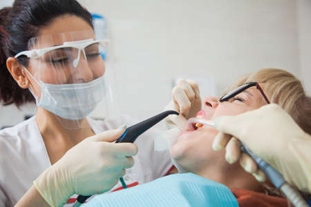 Closeup shot of dentist in protection mask working with tooth cavity and plague. Patient on stomatology chair repair aching teeth. Stomatologist and patient at clinic office. Toothcare conceptの写真素材