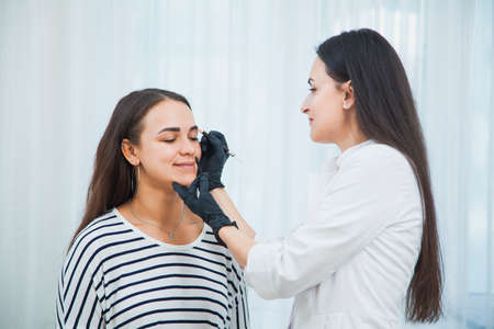 Beautician making eyebrows correction with special instruments. Young woman making beauty facial procedure.の写真素材