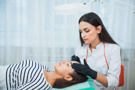 Permanent make-up for eyebrows in beauty salon. Beautician tattooing brows of a young woman. Eyebrow Correction. Beauty Concept.の写真素材