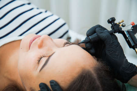 Young woman on permanent make-up procedure, tattooing eyebrows in natural tint. Eyebrow Correction closeup. Beauty Concept.の写真素材