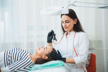 Permanent make-up for eyebrows in beauty salon. Beautician tattooing brows of a young woman. Eyebrow Correction. Beauty Concept.の写真素材