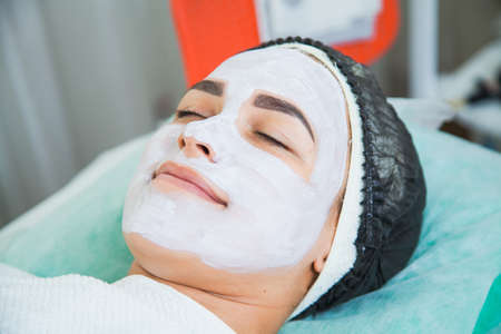 Closeup of woman face in white clay mask procedure in beauty salon. Face peeling mask, spa beauty treatment, skincare concept.の写真素材