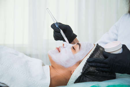 Closeup of woman face in white clay mask procedure in beauty salon. Face peeling mask, spa beauty treatment, skincare concept.の写真素材