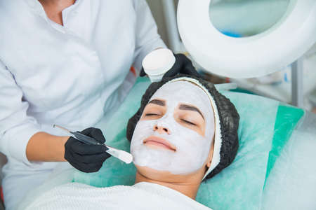 Closeup of woman face in white clay mask procedure in beauty salon. Face peeling mask, spa beauty treatment, skincare concept.の写真素材