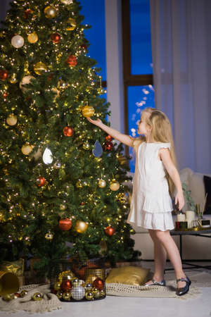 Cute little girl decorating christmas tree on New Years eve. Vertical photo of female child in festive room with xmas fir tree at night.の写真素材