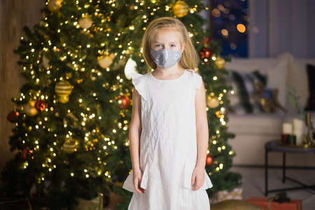 Little girl in protective mask and santas hat in decorated christmas room. New Years eve staying at home during covid lockdown.の写真素材