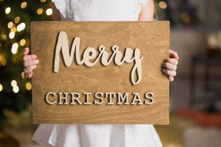7 year old girl holding wooden merry christmas placard. New year holidays concept.の写真素材