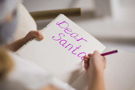 Happy little girl writing letter to Santa in decorated christmas room. Child smile and wish gifts near festive xmas fir-tree. New Year and winter holidays concept.の写真素材