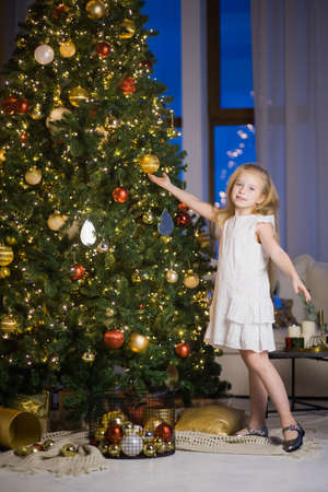 Cute little girl decorating christmas tree on New Years eve. Vertical photo of female child in festive room with xmas fir tree at night.の写真素材