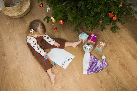 Little toddler girl sit on floor and write or draw letter for santa. Cute kid make wish on Christmas time at home.の写真素材