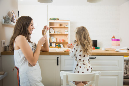 Young mother taking photo of her child decorating gingerbread cookies. Mom and daughter together at kitchen on Christmas timeの写真素材