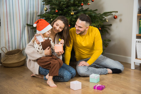 Happy winter holidays and Merry Christmas, dad, mom and little daughter exchange gifts near fir tree. New years Eve family at home.の写真素材