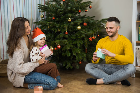 Happy winter holidays and Merry Christmas, dad, mom and little daughter exchange gifts near fir tree. New years Eve family at home.の写真素材