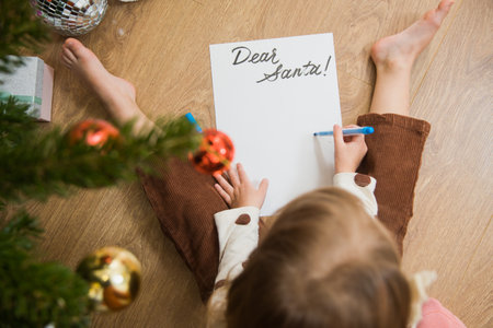 Little toddler girl sit on floor and write or draw letter for santa. Cute kid make wish on Christmas time at home.の写真素材
