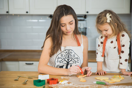 Mom and todddler daughter baking gingerbread cookies for Christmas. Decorating homemade biscuits for winter holidays.の写真素材