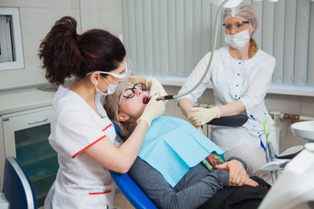 Closeup shot of dentist in protection mask working with tooth cavity and plague. Patient on stomatology chair repair aching teeth. Stomatologist and patient at clinic office. Toothcare conceptの写真素材