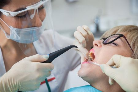 Dentist in protection mask washing mouth from tooth dust and blood. Patient on stomatology chair repair aching teeth. Stomatologist and patient at clinic office. Toothcare conceptの写真素材