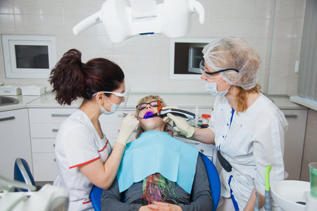Closeup shot of dentist and assistant in protection mask working with tooth cavity and plague. Patient repair aching teeth. Stomatologist and patient at clinic office. Toothcare conceptの写真素材