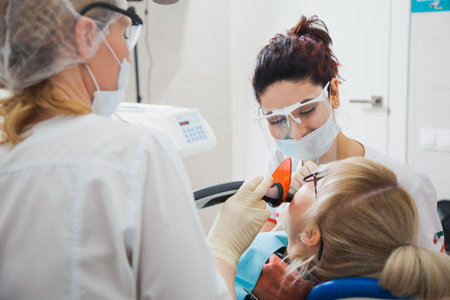 Closeup shot of dentist and assistant in protection mask working with tooth cavity and plague. Patient repair aching teeth. Stomatologist and patient at clinic office. Toothcare conceptの写真素材