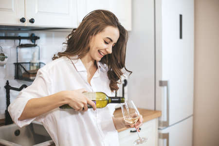 Young woman with glass of wine at home. Female person relax drinking wine at kitchen.の写真素材