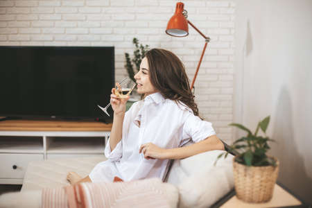Young woman with glass of wine at home. Female person relax drinking wine.の写真素材