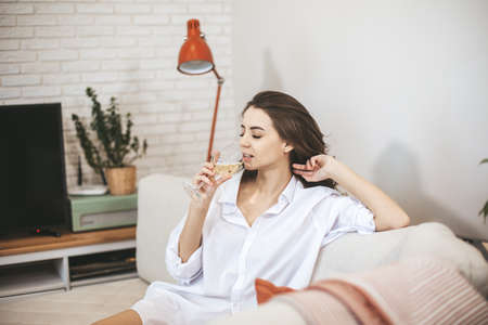 Young woman with glass of wine at home. Female person relax drinking wine.の写真素材