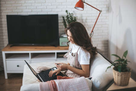 Young millennial woman shopping online at home. Female person using laptop and credit card to buy new things.の写真素材