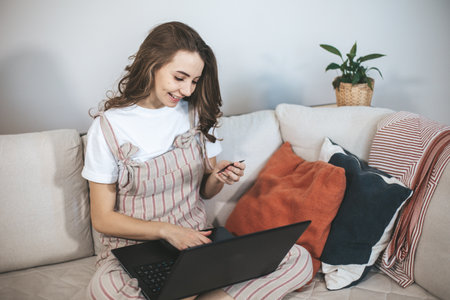 Young millennial woman shopping online at home. Female person using laptop and credit card to buy new things.の写真素材