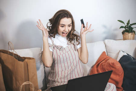 Young millennial woman shopping online at home. Female person using laptop and credit card to buy new things.の写真素材